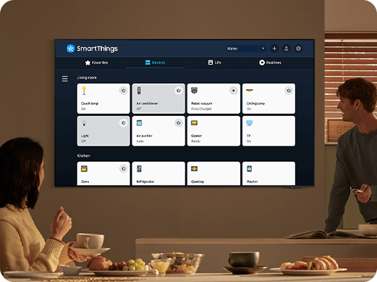 Dos personas miran la pantalla de la TV 2024 Samsung OLED y controlan sus dispositivos con la app SmartThings que hace que su casa sea inteligente.
  