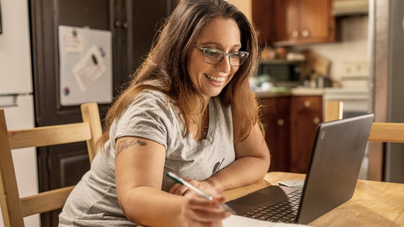 Una mujer que trabaja sentada en su escritorio con una laptop, sonriendo.