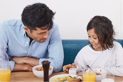 Pai e filha olhando juntos para um produto do Google durante o café da manhã.
