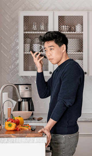 Un homme asio-américain se tient près d'un plan de travail dans une cuisine et tient son smartphone Android près de son oreille.
