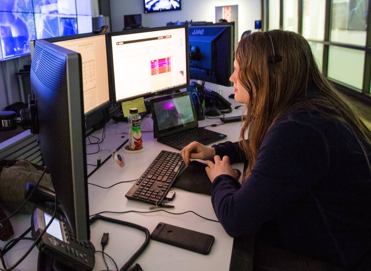 Wanita muda yang bekerja di meja kerja di depan tiga monitor.