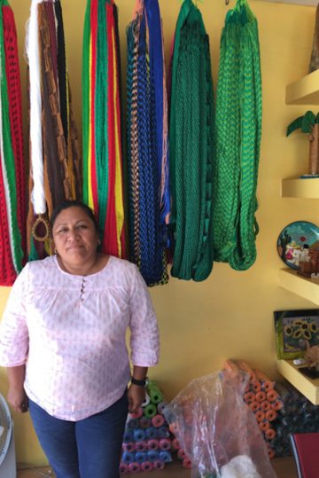 A portrait of Irene, a woman wearing a yellow sleveless top, gazing at the camera against a rainbow backdrop of woven textiles.