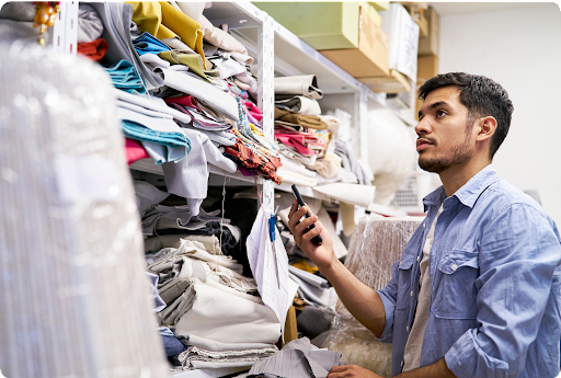 A worker comparing a swatch on his phone to a wall of colorful textiles.