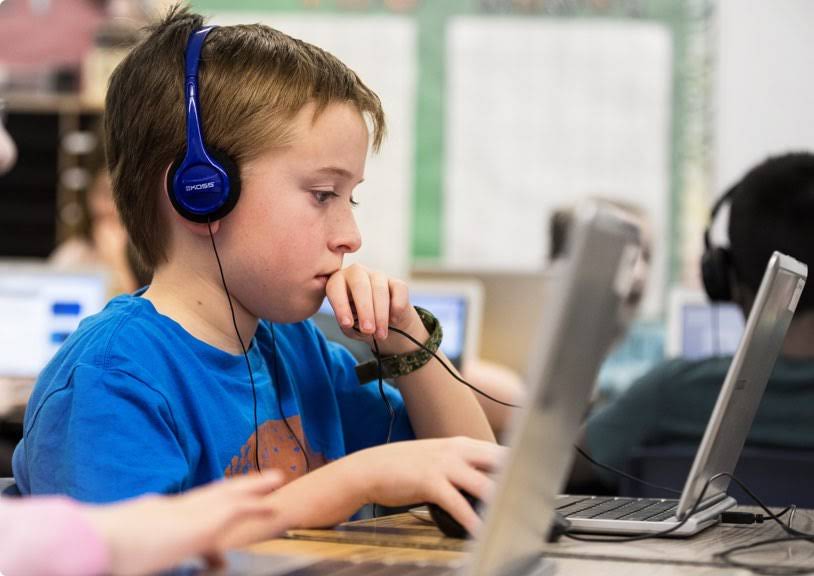 Seorang anak menggunakan Chromebook dengan headphone.