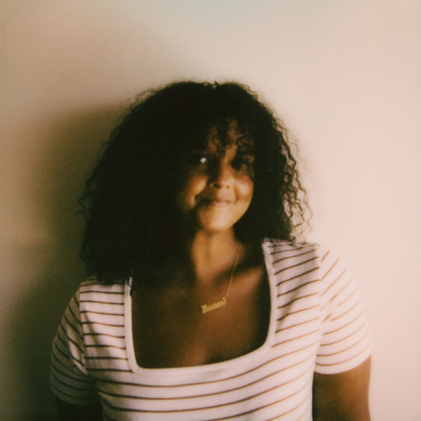 Portrait of artist in a striped brown and cream scoop neck top in front of a beige background.