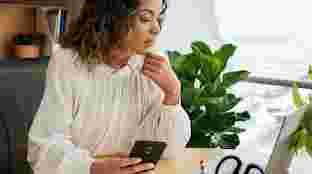 A Black man in blue scrubs wearing a stethoscope reviewing data on a tablet with a Black, female doctor in white scrubs in a healthcare center.