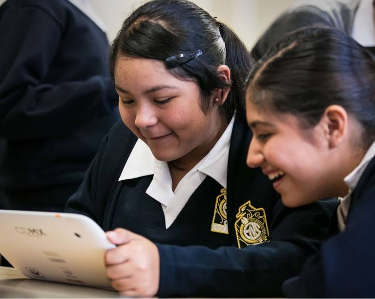 Kaksi koulupukuun pukeutunutta tyttöä hymyilee tabletin äärellä