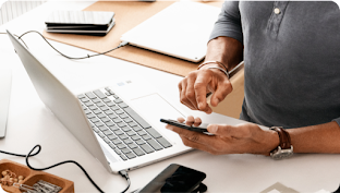 Man sits at desk, scrolling on his mobile phone with his index finger.