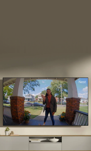 A TV in a living room showing a delivery person standing on a stoop waving to the doorbell camera.