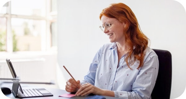 Eine lächelnde Frau, die an einem Meet-Anruf teilnimmt und sich Notizen macht 