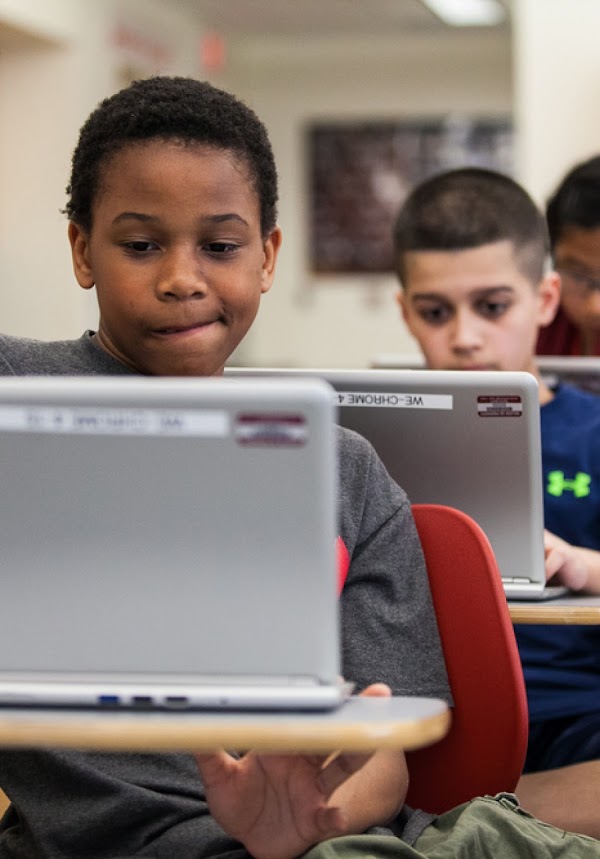 Dos jóvenes en un salón de clases trabajan en sus computadoras portátiles