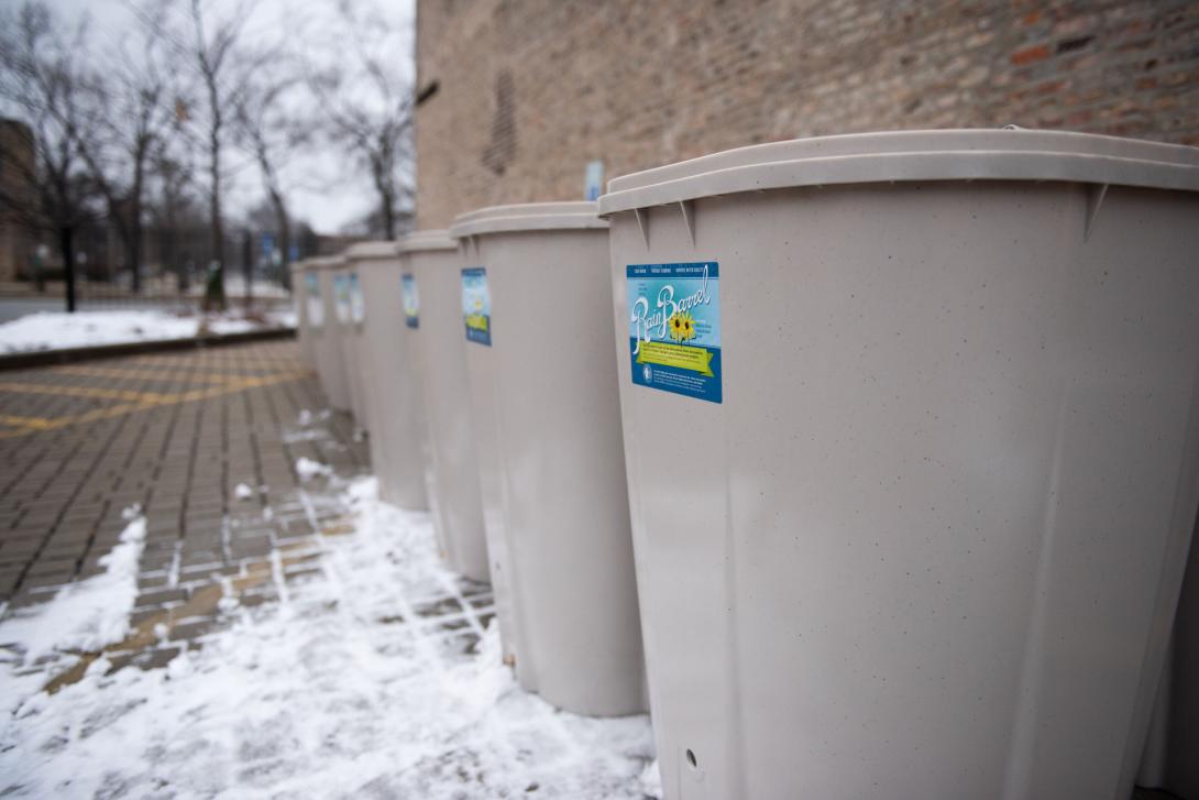 A row of squared-off rain barrels on a snowy permeable paver parking lot