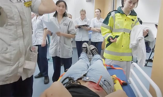 A photo from a major incident simulation; a patient with a fake injury is wheeled into hospital as students take on different nursing roles 