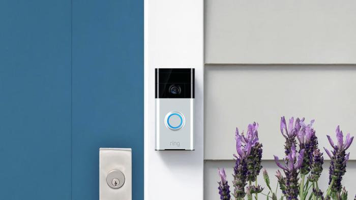 A Ring doorbell camera mounted on the frame of a blue door next to some flowers.