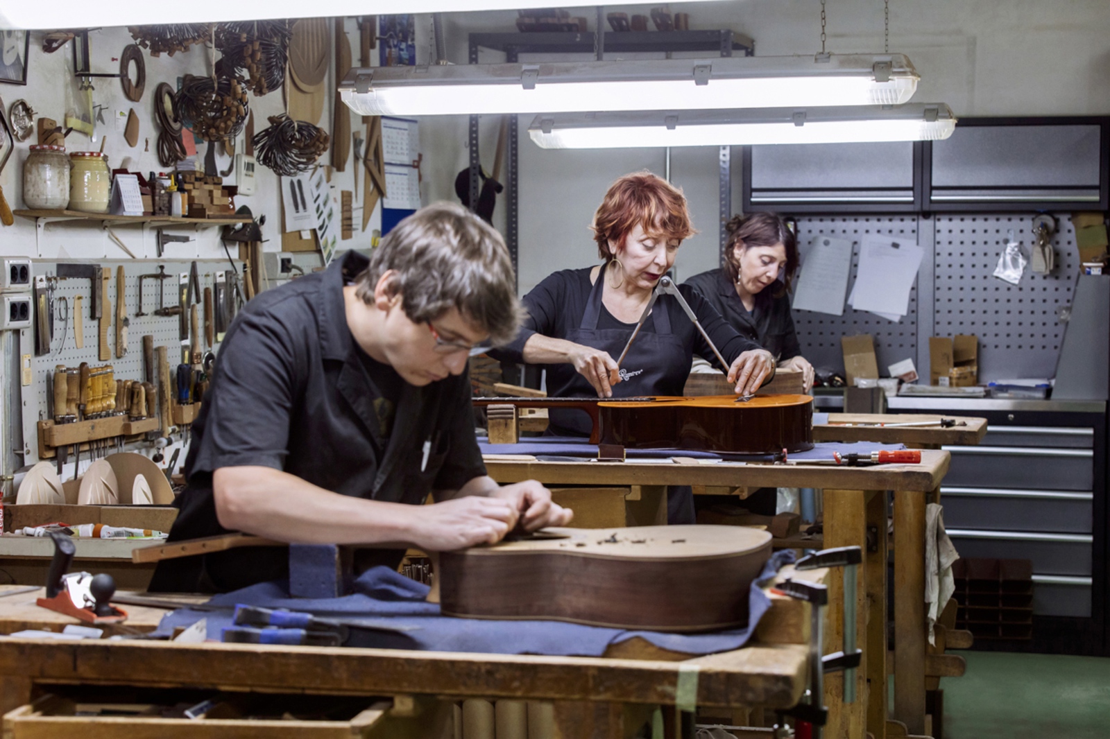 Bir gitar imalat firmasından üç zanaatkar, ahşap iş tezgahlarında gitar parçalarını şekillendiriyor.